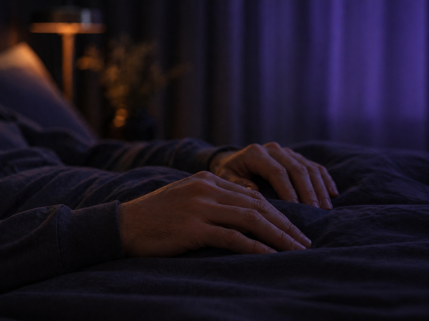 Close de maos relaxadas sobre um cobertor escuro com luz violeta suave.